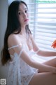 A woman sitting on a window sill holding a flower.